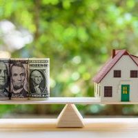 Home loan / reverse mortgage or transforming assets into cash concept : House model, US dollar notes on a simple balance scale, depicts a homeowner or a borrower turns properties / residence into cash